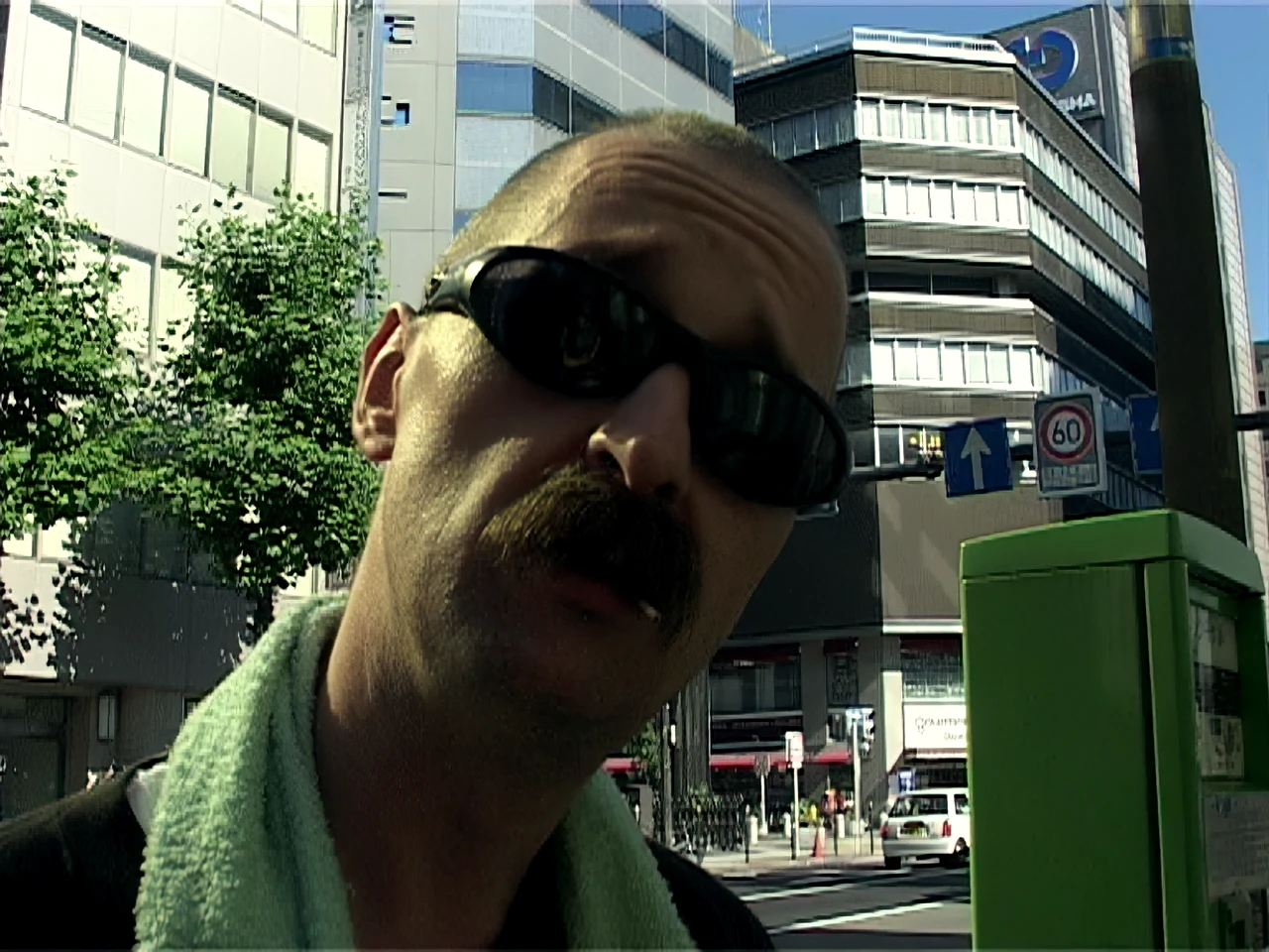 Alfred in wraparound sunglasses, a green towel round his neck, on an Osaka street